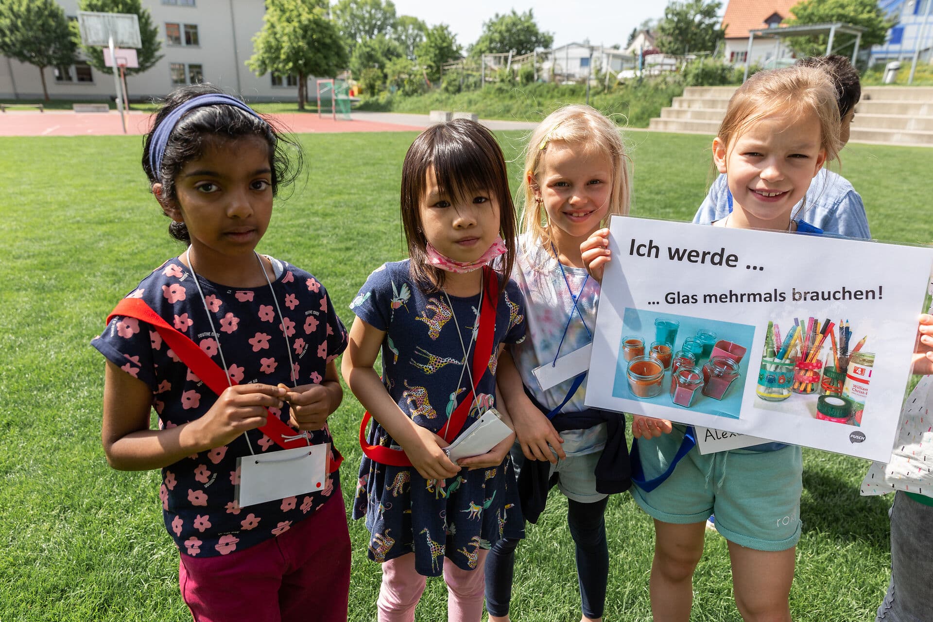 Mädchen stehen auf einer Wiese und halten ein Plakat, auf dem steht «Ich werde Glas mehrmals brauchen»